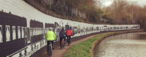 Three people riding their bike along a canal.